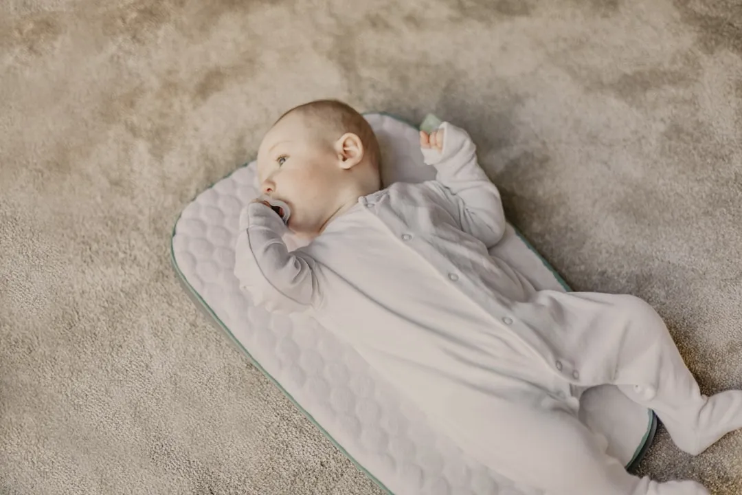 baby in white onesie lying on white and blue bed
