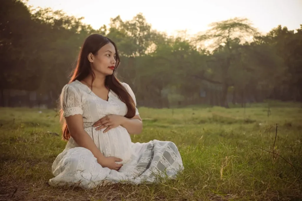 A pregnant woman sitting in a field at sunset