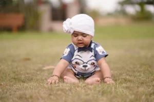 A baby sitting in the grass wearing a white hat