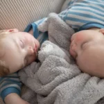 a couple of babies laying next to each other on a couch