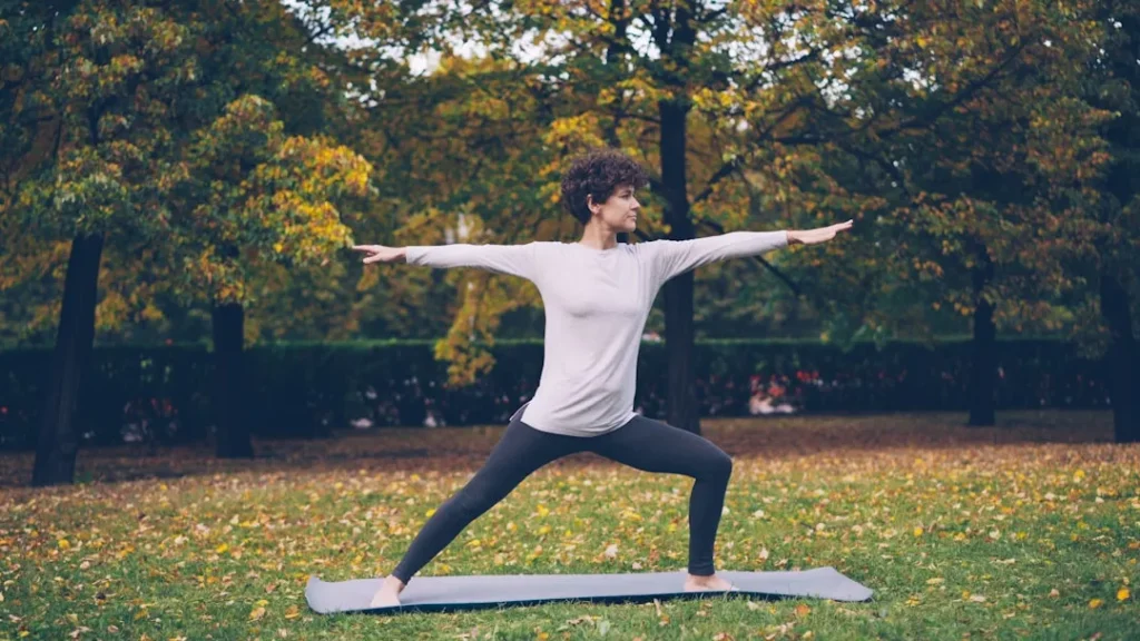 Woman practicing yoga warrior pose in autumn park.