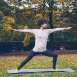 Woman practicing yoga warrior pose in autumn park.