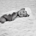 grayscale photo of baby lying on white textile