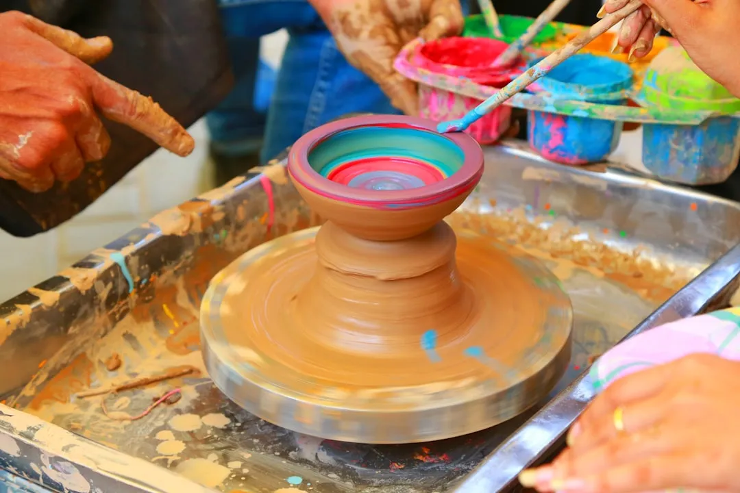 Hands painting a clay pot on a spinning wheel