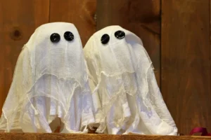Two fabric ghosts with button eyes on a shelf