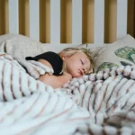 a little girl sleeping in a bed with a blanket