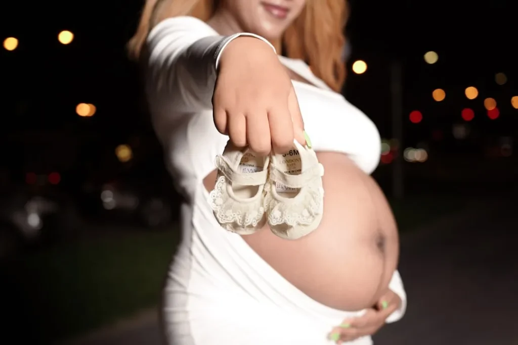 A pregnant woman holding a pair of baby shoes