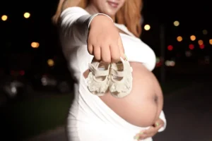 A pregnant woman holding a pair of baby shoes