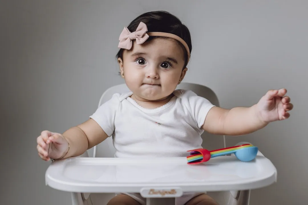 A baby sitting in a high chair with a bow on her head