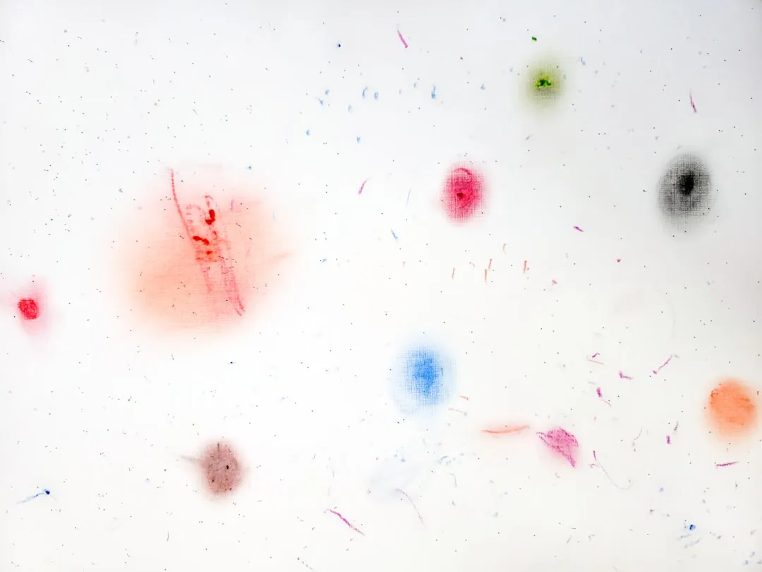 White surface with colorful, blurred paint spots and faint lines.