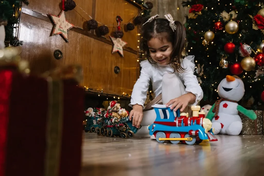 A little girl playing with a toy train in front of a christmas tree
