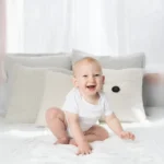 smiling baby sitting on white bed