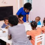 Teacher guiding children drawing at a table.