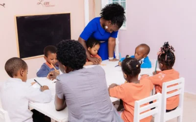 Teacher guiding children drawing at a table.