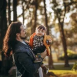 woman in blue denim jacket carrying baby in black and white striped long sleeve shirt during