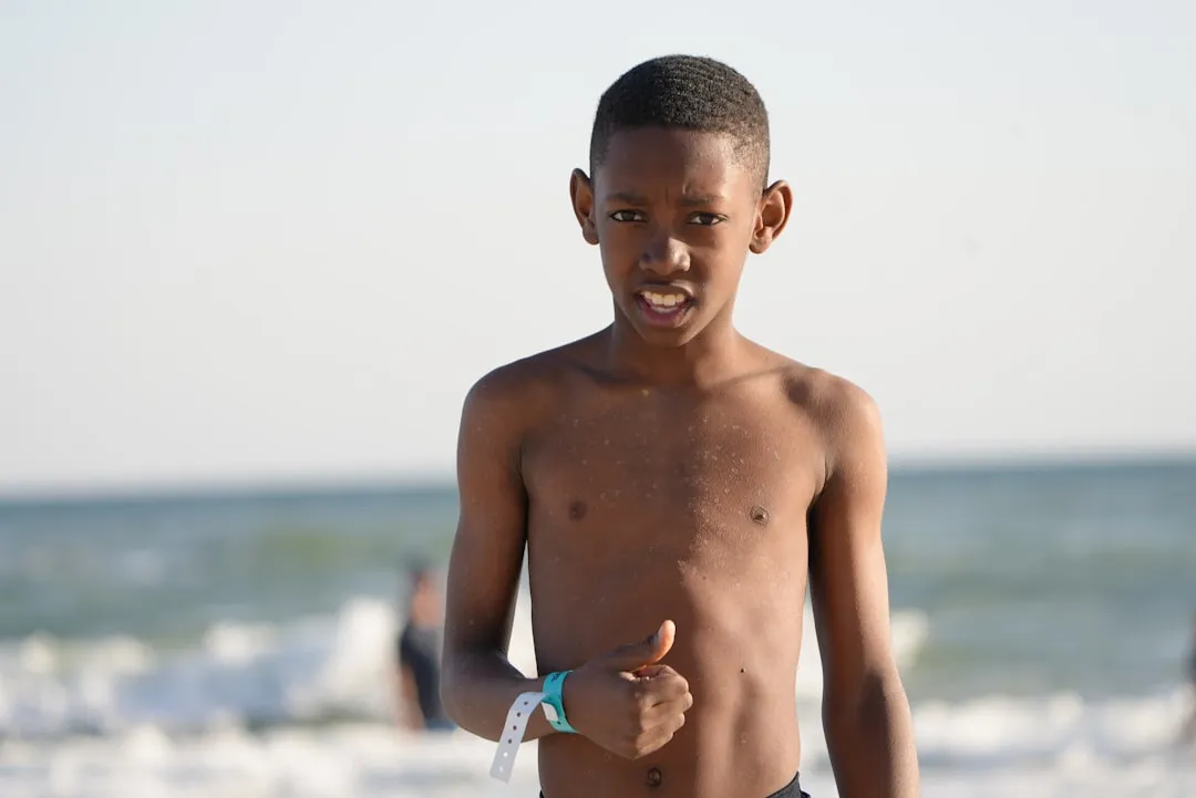 a young boy standing on top of a beach next to the ocean