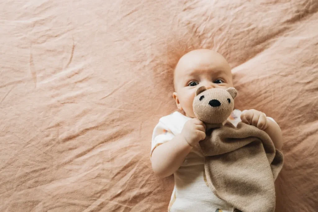 A baby laying on a bed with a teddy bear